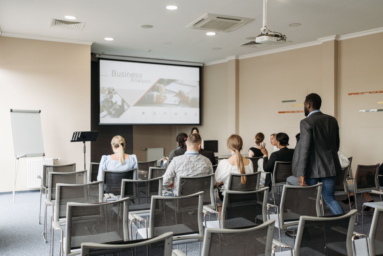 Business conference attendees listening to a presentation in an office setting.